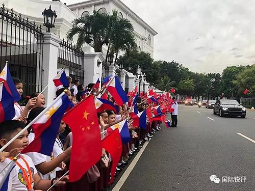 20日，来自马尼拉当地三所小学的千名小学生站在总统府道路两侧挥舞两国国旗，欢迎习主席车队。（图片来源：中央广播电视总台央视新闻 记者邓雪梅拍摄）